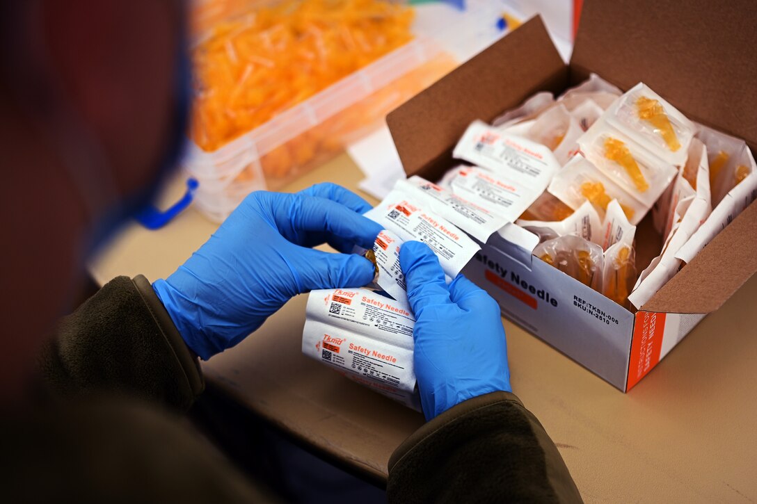 An airman wearing gloves unpacks needles.