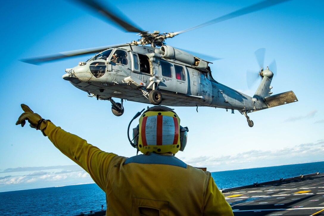 Helicopter hovers over an aircraft carrier.