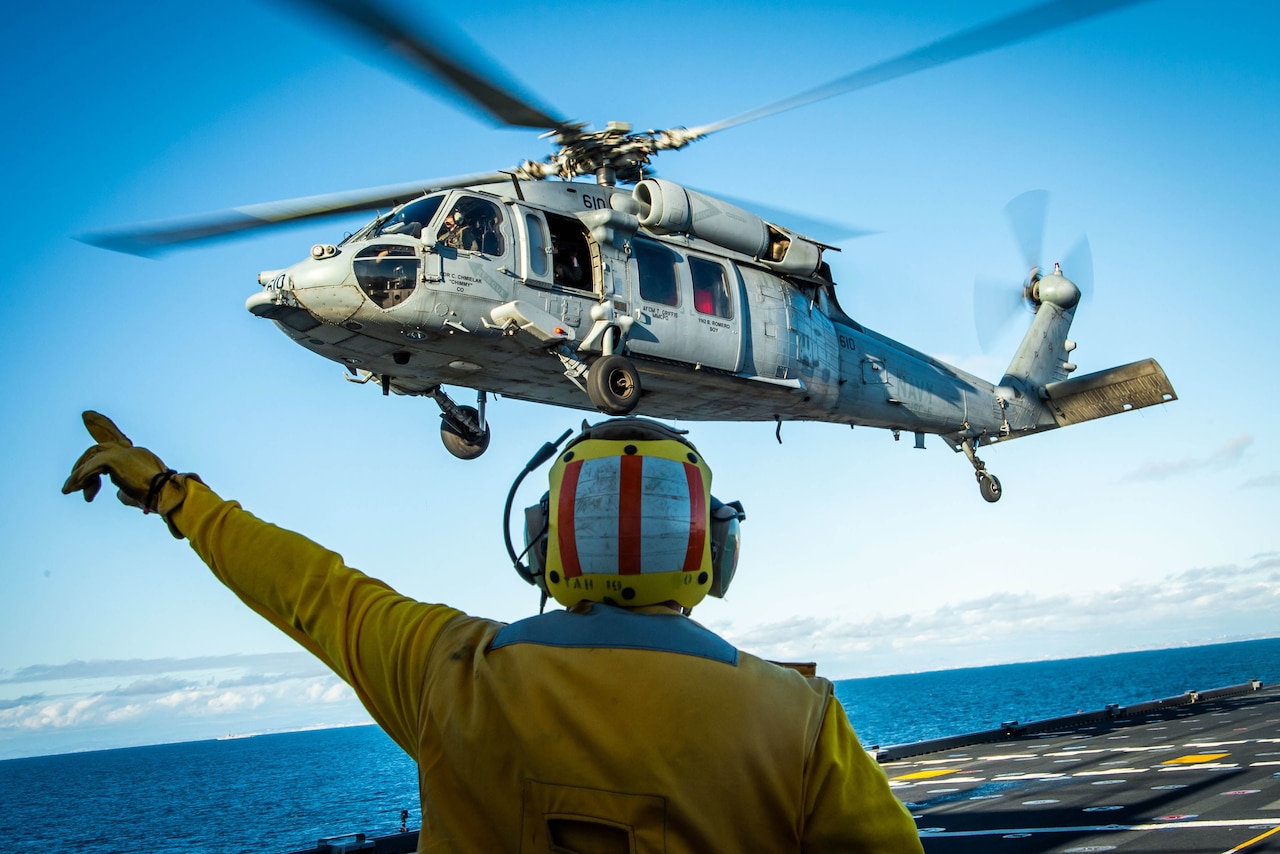 Helicopter hovers over an aircraft carrier.