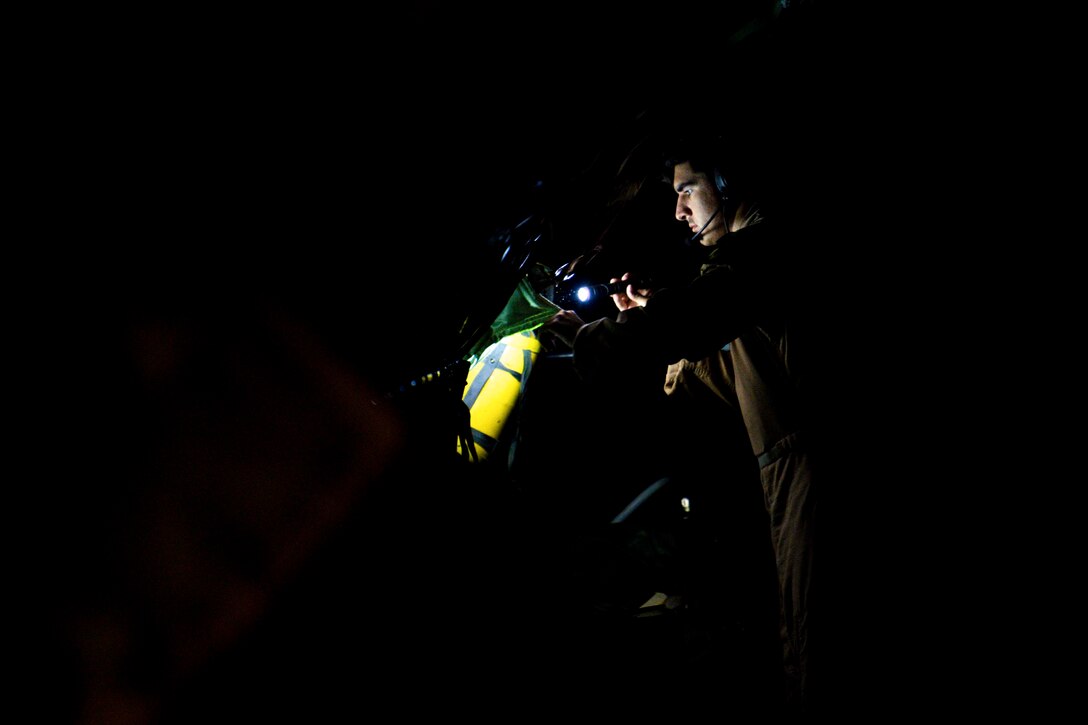 An airman uses a small flashlight inside a dark aircraft.