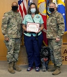Brooke Army Medical Center Commanding General Brig. Gen. Shan Bagby and Command Sgt. Maj. Thurman Reynolds present Kris Blair and therapy dog Huckleberry are certificate of appreciation.