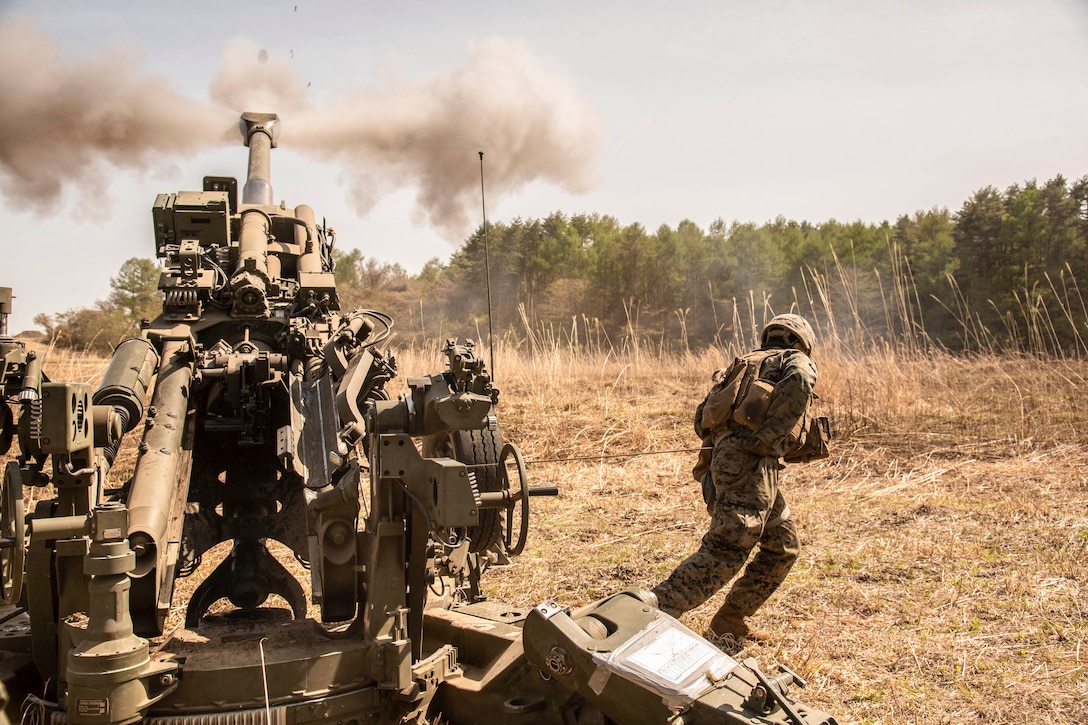 A Marine fires a howitzer toward a tree line.