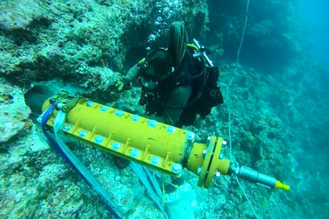 A sailor wearing diving gear works with equipment underwater.