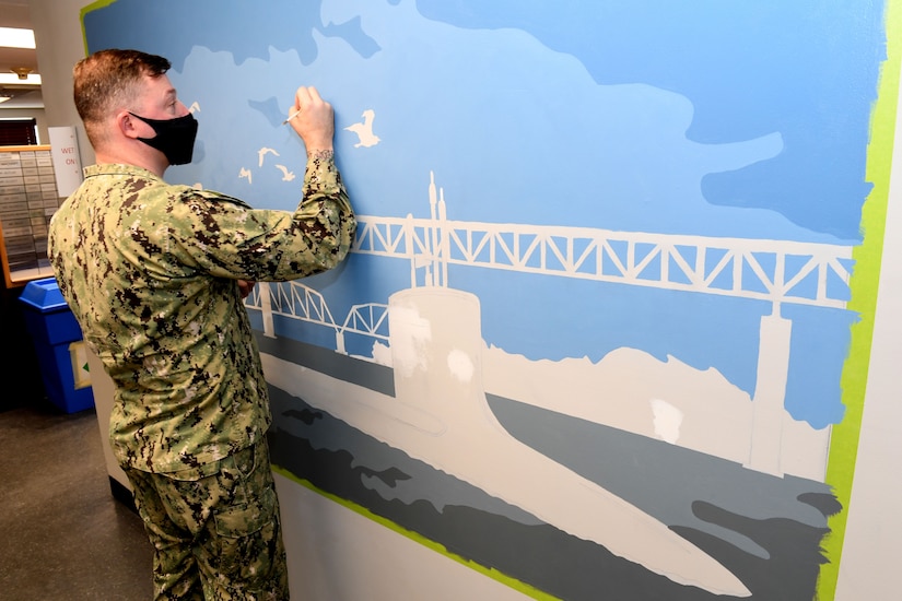 A sailor paints a mural on a wall.