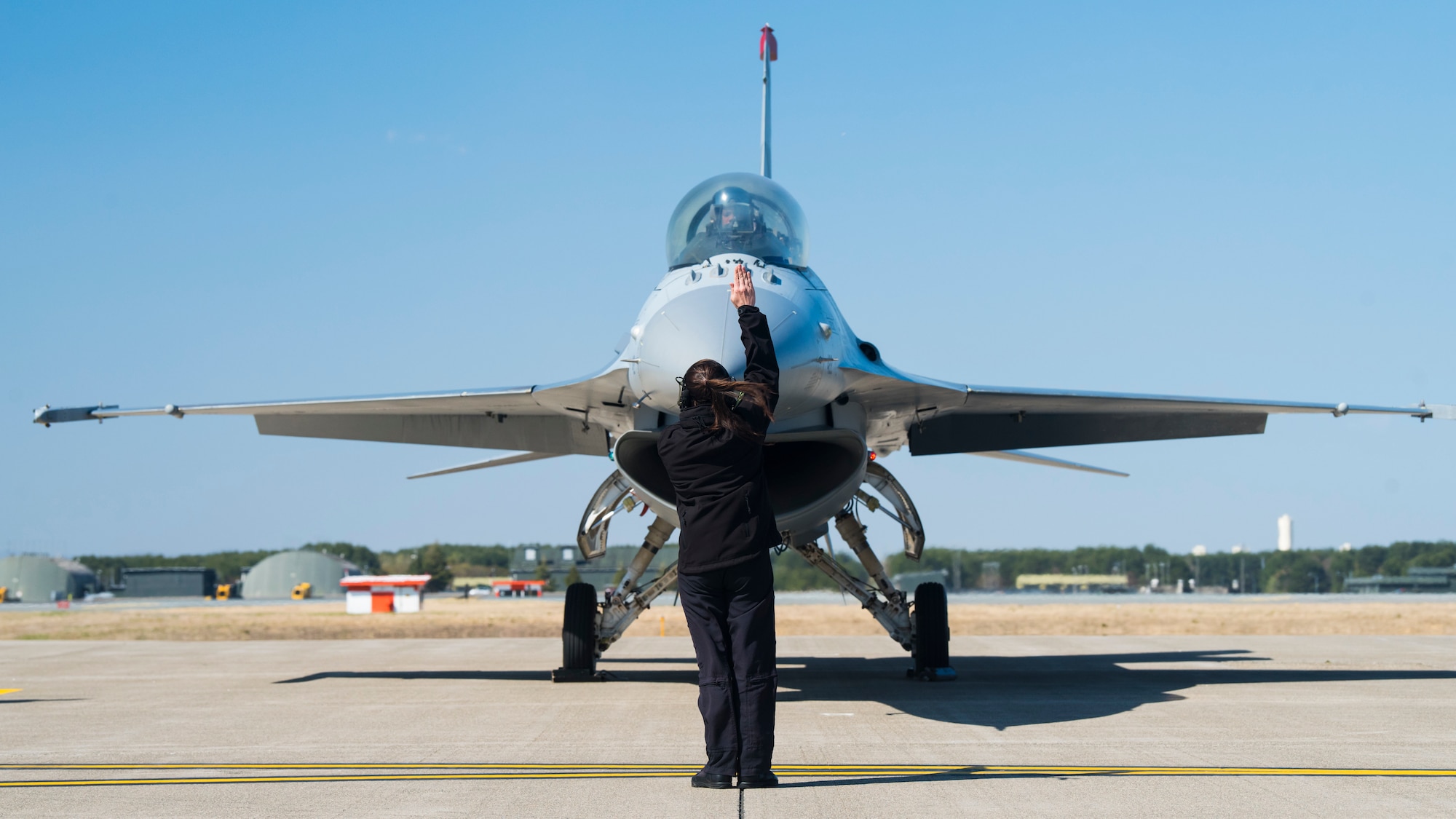 Air Force member giving hand signals in front of F-16.