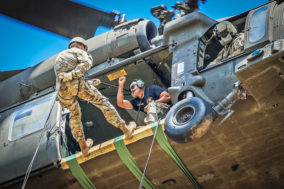Soldiers ready to rappel from a hovering helicopter.