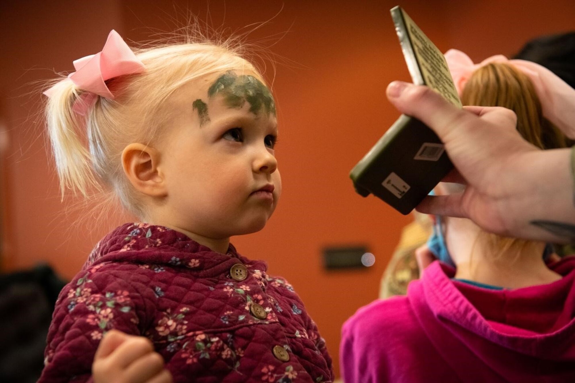Ennsley, a military child, checks herself in a mirror after having camouflage paint applied to her forehead at the Kid’s Deployment Line event on Ellsworth Air Force Base, S.D., April 17, 2021.