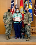 General Brig. Gen. Shan Bagby and Command Sgt. Maj. Thurman Reynolds present Kris Blair and therapy dog Huckleberry a certificate of appreciation for their volunteer service.
