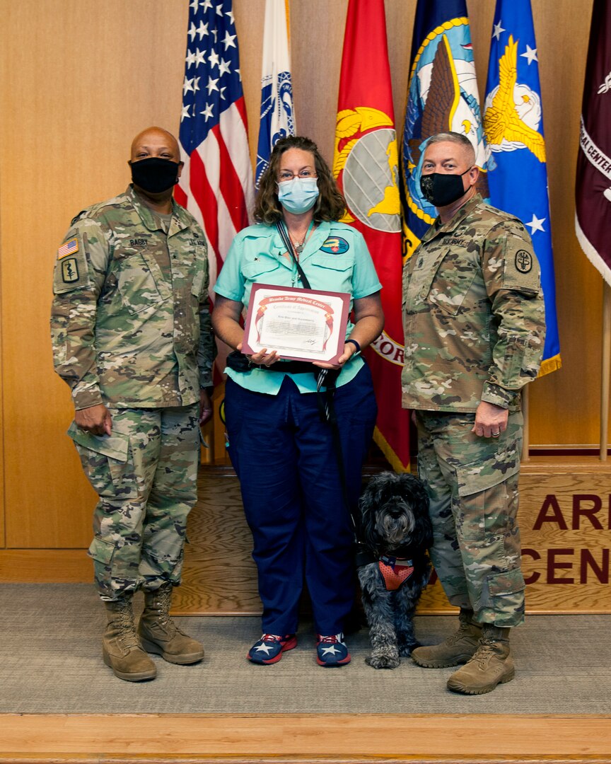 General Brig. Gen. Shan Bagby and Command Sgt. Maj. Thurman Reynolds present Kris Blair and therapy dog Huckleberry a certificate of appreciation for their volunteer service.