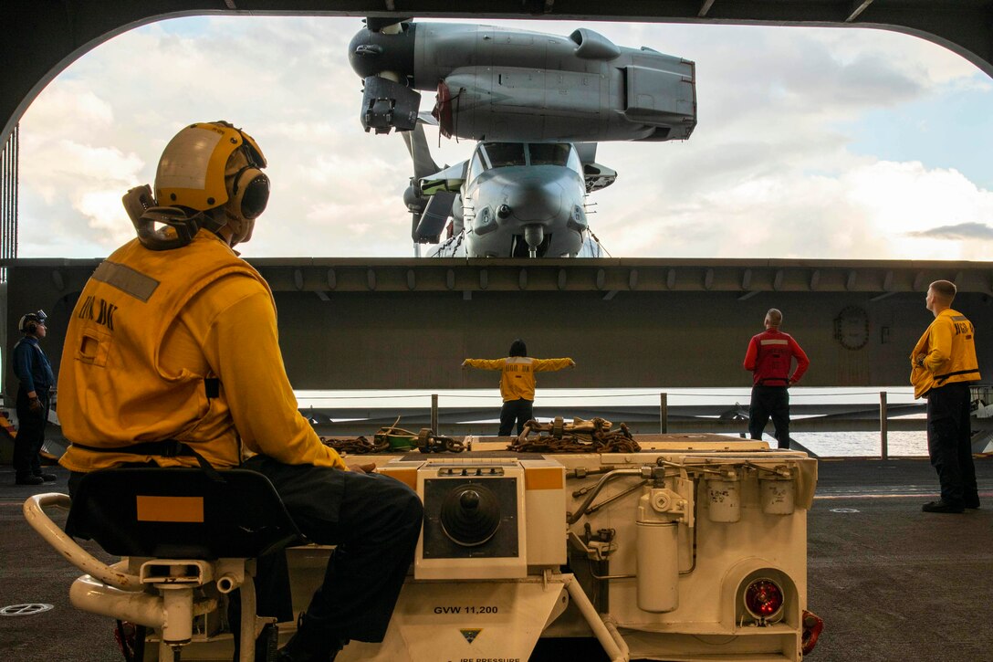 Sailors watch as an aircraft moves onto a ship at sea.