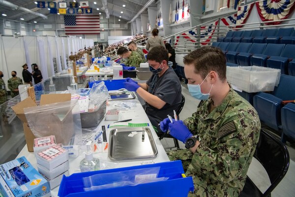 Hospital corpsman and healthcare workers from Captain James A. Lovell Federal Health Care Center prepare COVID 19 vaccinations for recruits in Pacific Fleet Drill Hall at Recruit Training Command.
