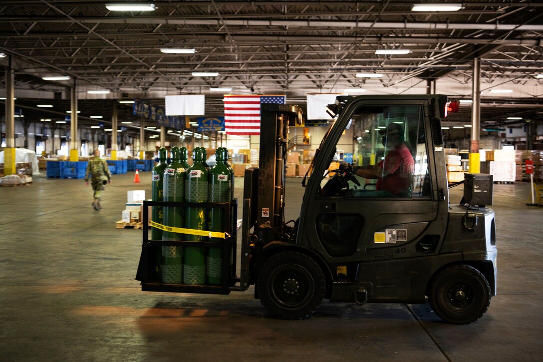 A man wearing a face mask operates a forklift to move oxygen tanks.