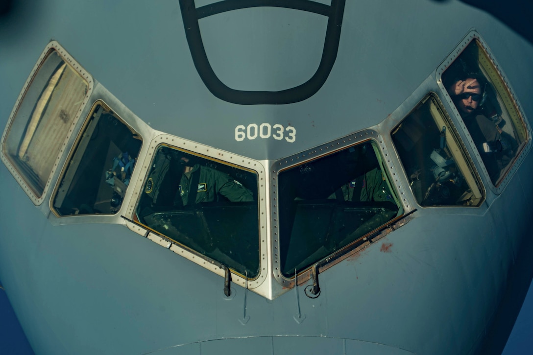 Airmen sit in the cockpit of an airborne aircraft.