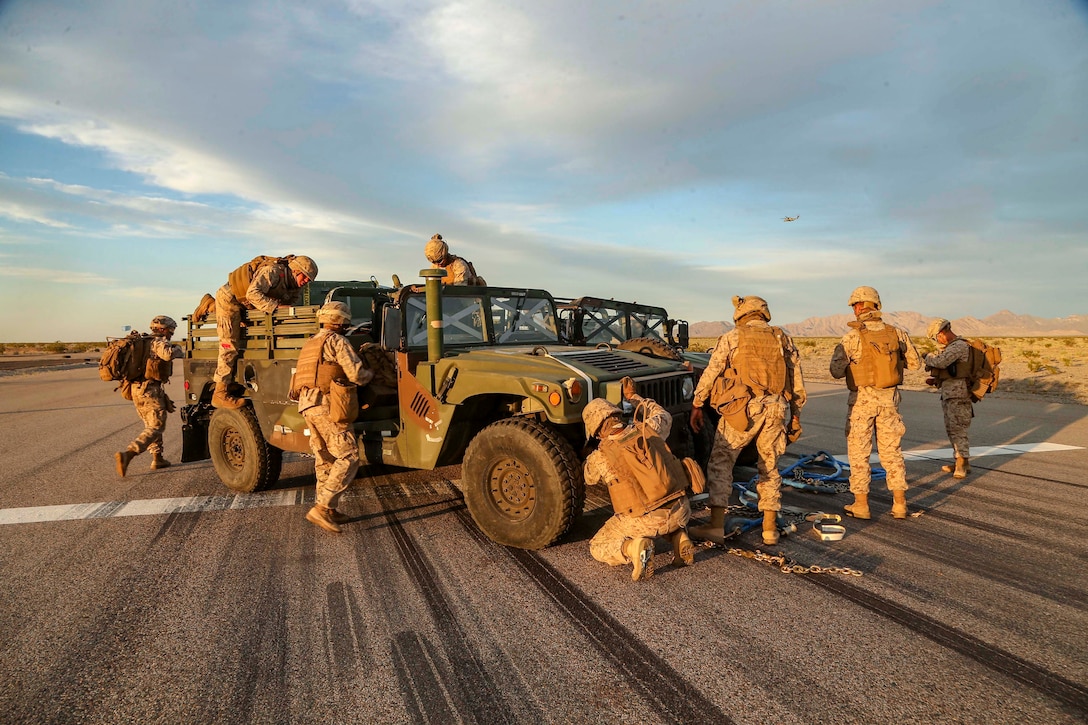 Marines work on vehicles in a desert.