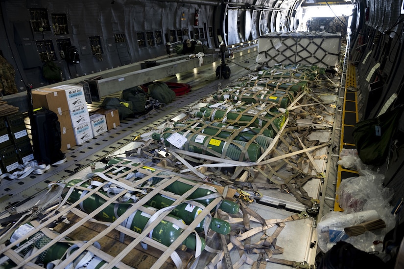 Inside a military aircraft, metal cylinders are attached to the floor with netting.