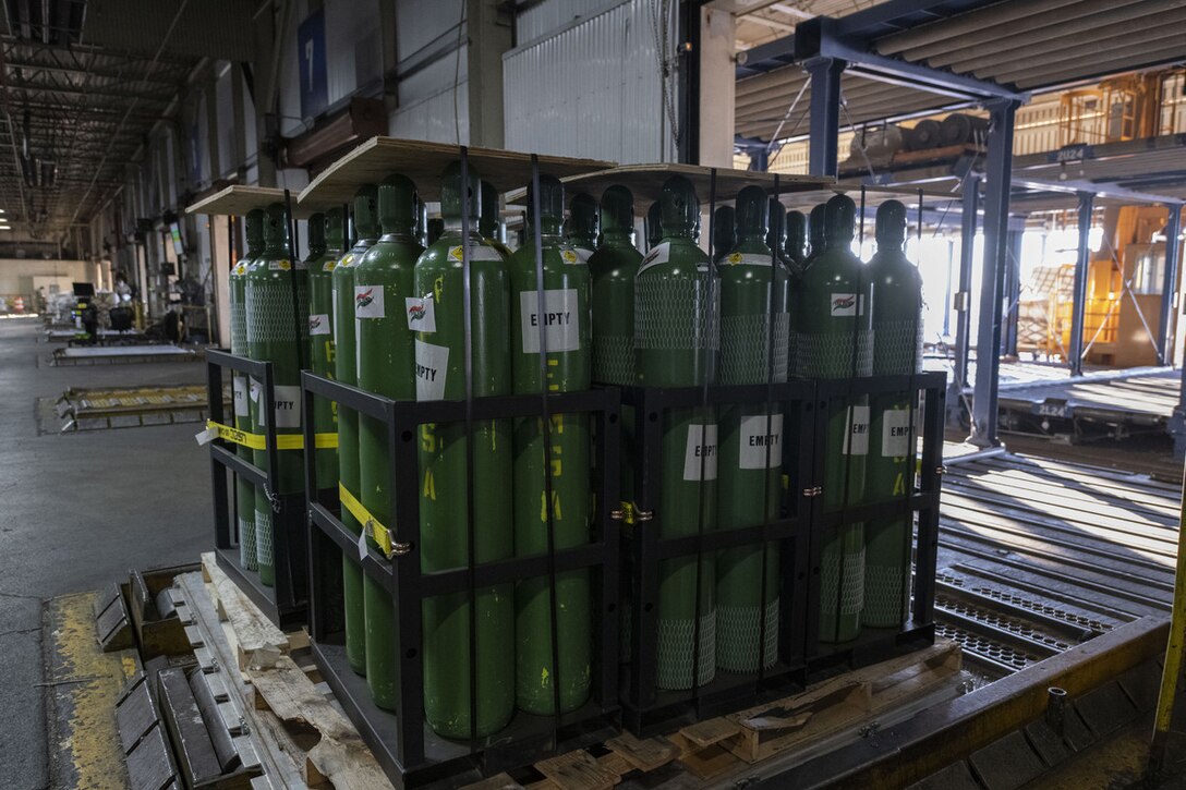 Dozens of metal oxygen cylinders sit on wooden pallets.