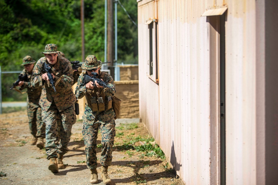 Marines move toward a door while holding up weapons.