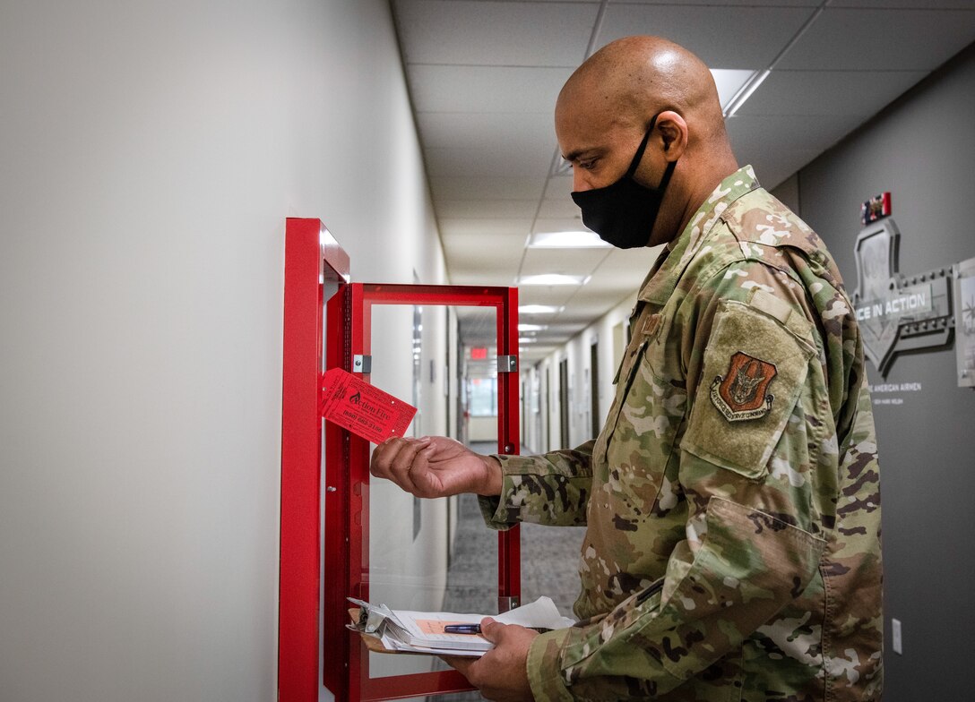 Man holds red paper tag while staring at fire extinguisher case.