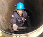 A woman in overalls climbs in to a ship's fuel tank