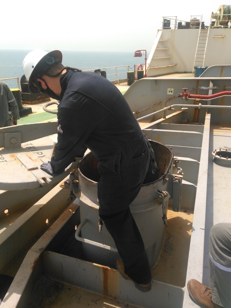 A man in overalls climbs in to a ship's fuel tank