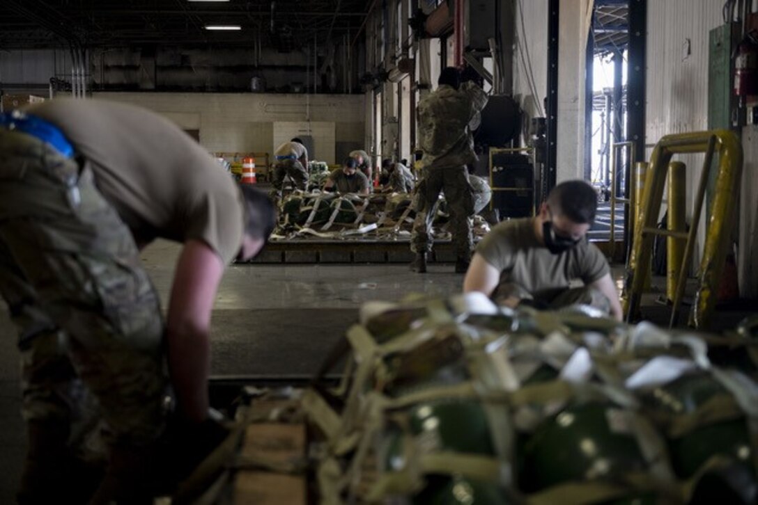 Airmen strap down pallets of cargo with webbing in a warehouse