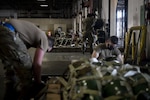 Airmen strap down pallets of cargo with webbing in a warehouse