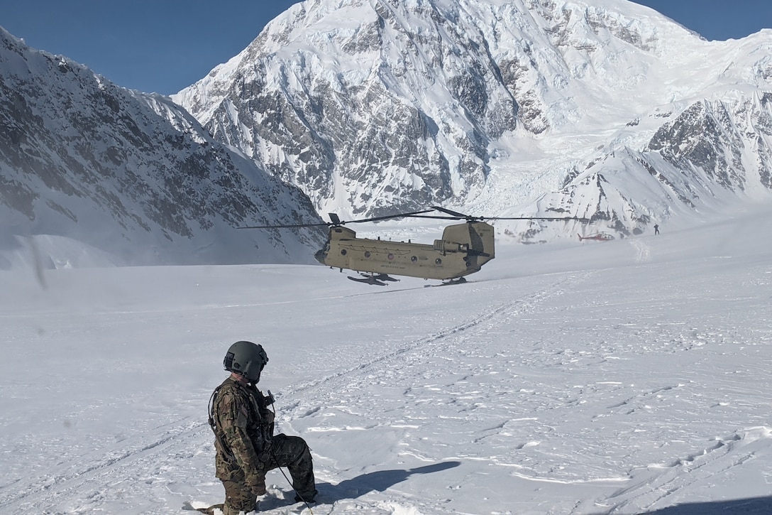 A soldier watches as a helicopter lands in the snow.