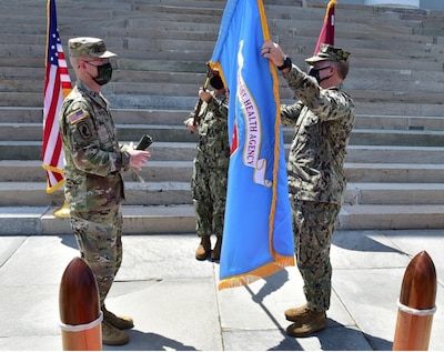 U.S. Army Lt. Gen. Ronald Place, director of the Defense Health Agency, left, and U.S. Navy Rear Adm. Darin K. Via, director of the Tidewater Market, and commander, Naval Medical Forces Atlantic, unfurl the Defense Health Agency flag during a socially distanced establishment ceremony to mark the standup of the Tidewater Market, April 28, 2021.