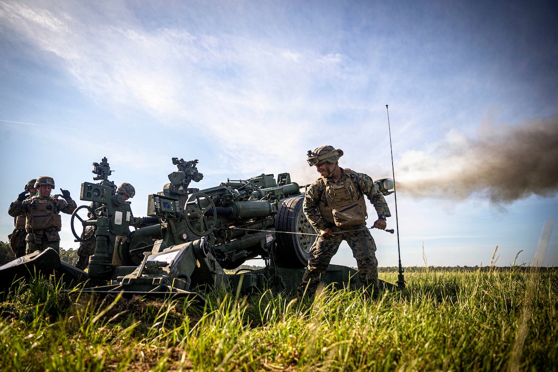 Marines fire a weapon in a field.