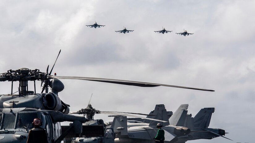 Four aircraft fly over a ship at sea.