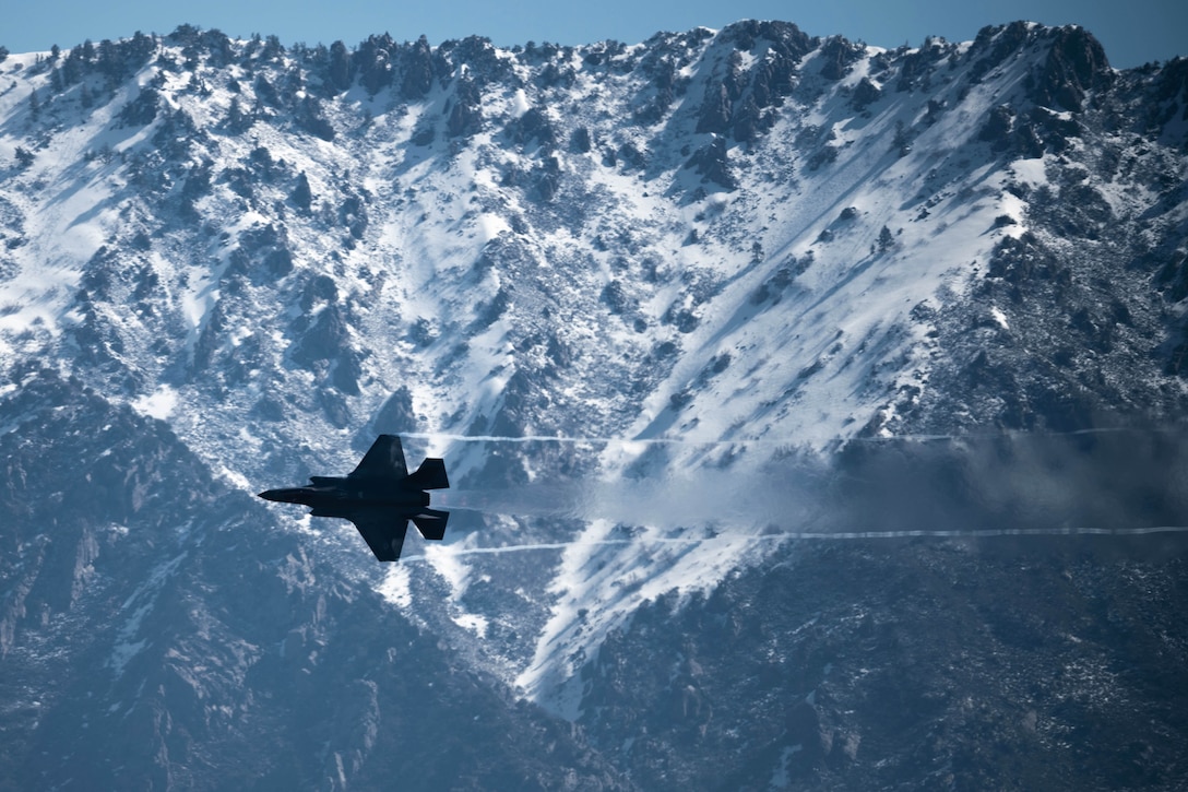 An aircraft flies by snowy mountains.