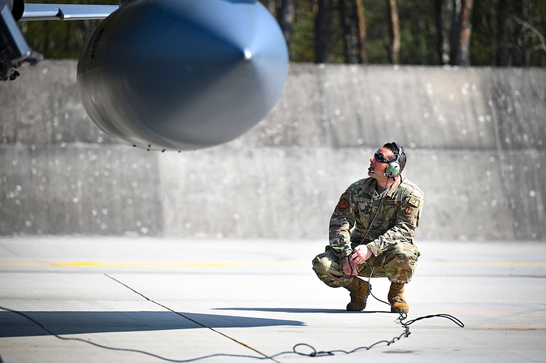 An airman kneels next to an Air Force aircraft.