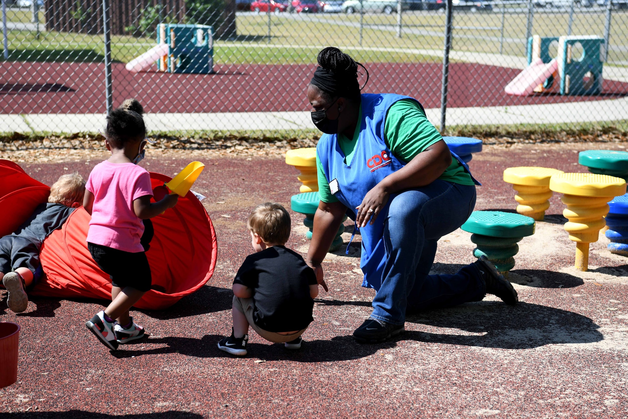 lady kneeling on playground with pre-kids