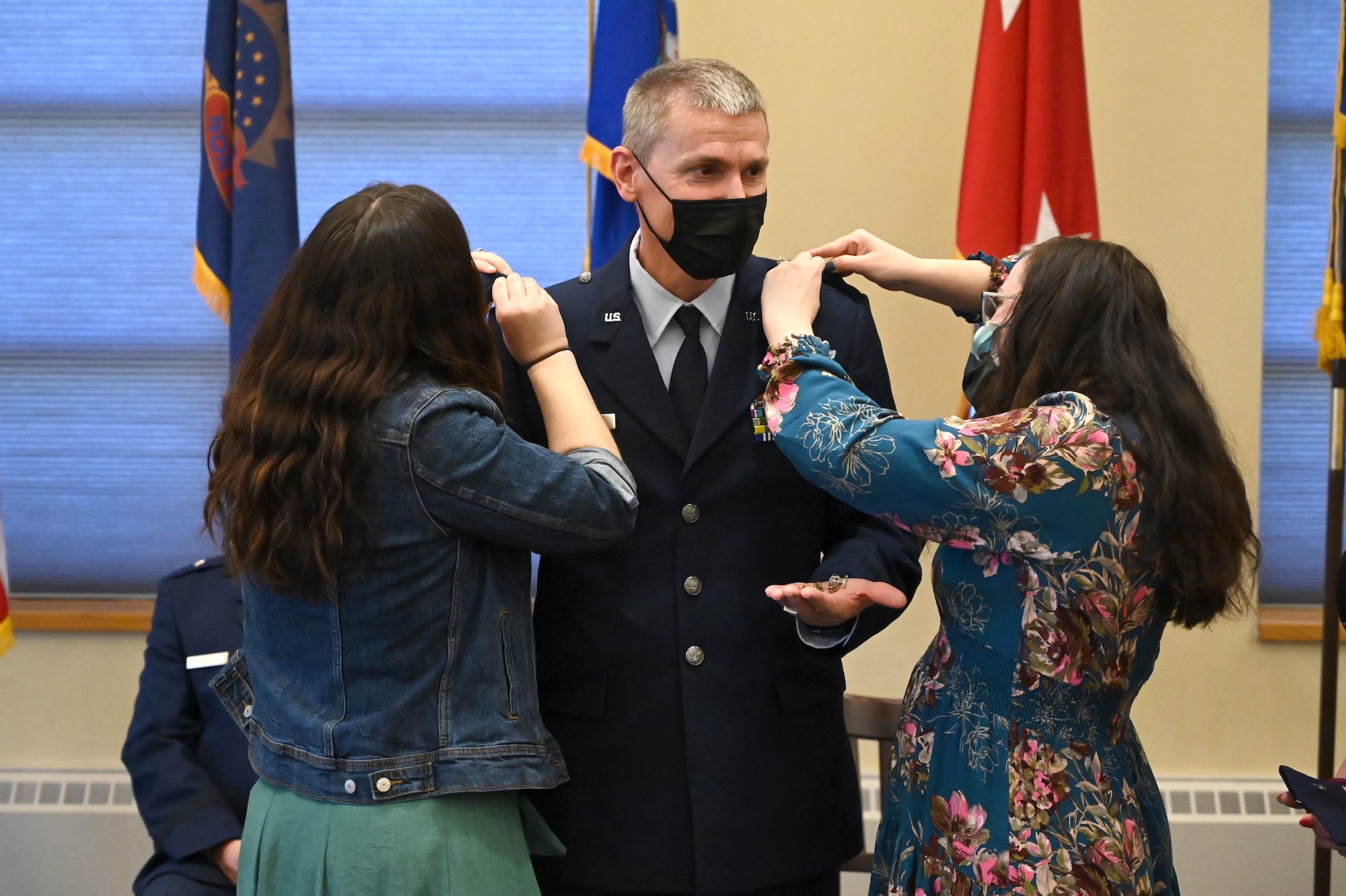 Brig. Gen. Darrin Anderson stands in service dress blue jacket between his daughters as they pin his new rank on the shoulders of his uniform.