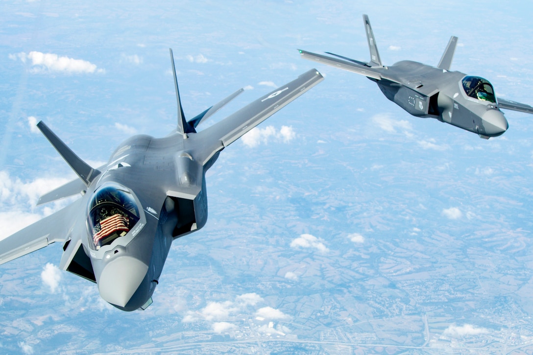 Two aircraft, one with a U.S. flag displayed in the cockpit, fly together.