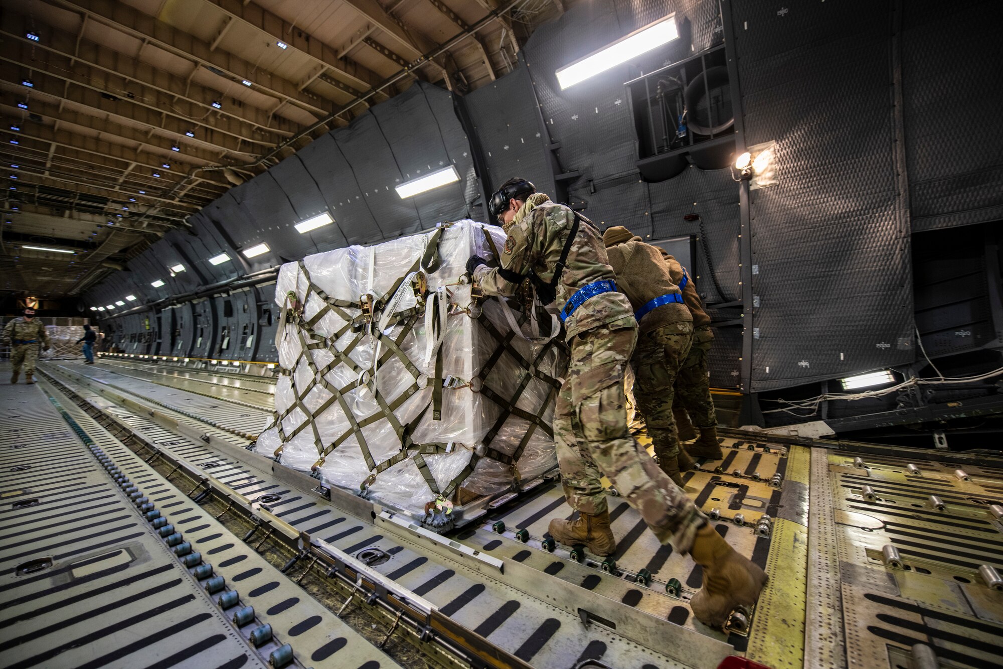 Airmen move pallets inside a large military aircraft.