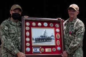 210729-N- IG466-0092 NAVAL SUPPORT ACTIVITY BAHRAIN (July 29, 2021) – Lt. Tabitha McAdams, left, presents Capt. Christopher Gilbertson, outgoing commander of Destroyer Squadron (DESRON) 50 and Task Force (TF) 55, with a farewell gift during a change of command ceremony presided over by Vice Adm. Brad Cooper, commander, U.S. Naval Forces Central Command, U.S. 5th Fleet and Combined Maritime Forces, onboard Naval Support Activity Bahrain, July 29. DESRON 50 and TF 55 operate in the U.S. 5th Fleet area of operations in support of naval operations to ensure maritime stability and security in the Central Region, connecting the Mediterranean and Pacific through the western Indian Ocean and three critical chokepoints to the free flow of global commerce. (U.S. Navy photo by Mass Communication Specialist 2nd Class Adelola Tinubu)