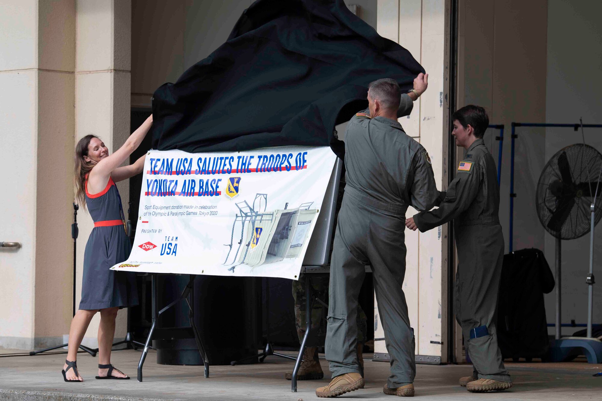Tristan Gale, left, 2002 Olympic gold medalist, helps Col. Andrew Campbell, center, 374th Airlift Wing commander, and Col. Julie Gaulin, right, 374th AW vice commander, unveil Team USA's contribution to Yokota Air Base, Japan, during the Olympic Salute July 30, 2021.