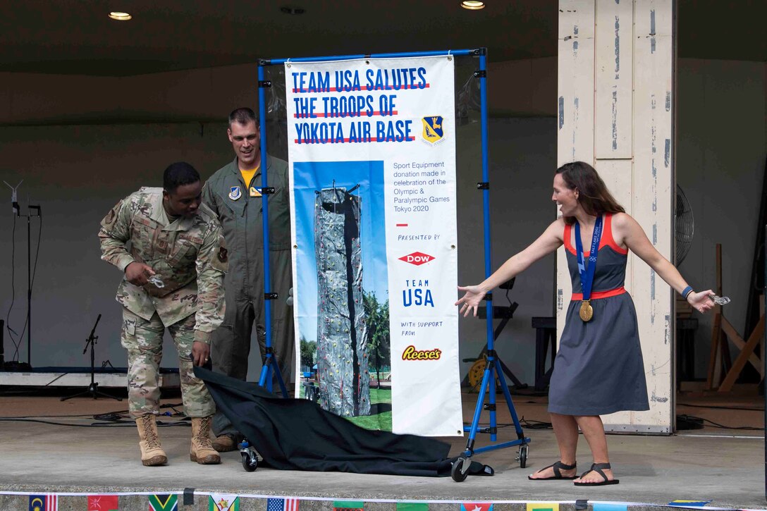 Chief Master Sgt. Jerry Dunn, left, 374th Airlift Wing command chief, Col. Andrew Campbell, center, 374th AW commander, and Tristan Gale, right, 2002 Olympic gold medalist, unveil a contribution from Team USA during the Olympic Salute at Yokota Air Base, Japan, July 30, 2021.