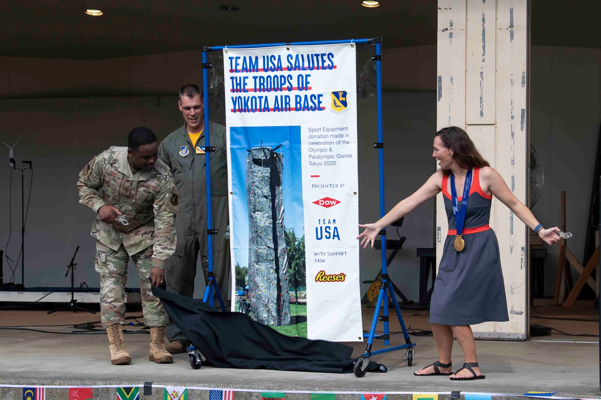 Chief Master Sgt. Jerry Dunn, left, 374th Airlift Wing command chief, Col. Andrew Campbell, center, 374th AW commander, and Tristan Gale, right, 2002 Olympic gold medalist, unveil a contribution from Team USA during the Olympic Salute at Yokota Air Base, Japan, July 30, 2021.