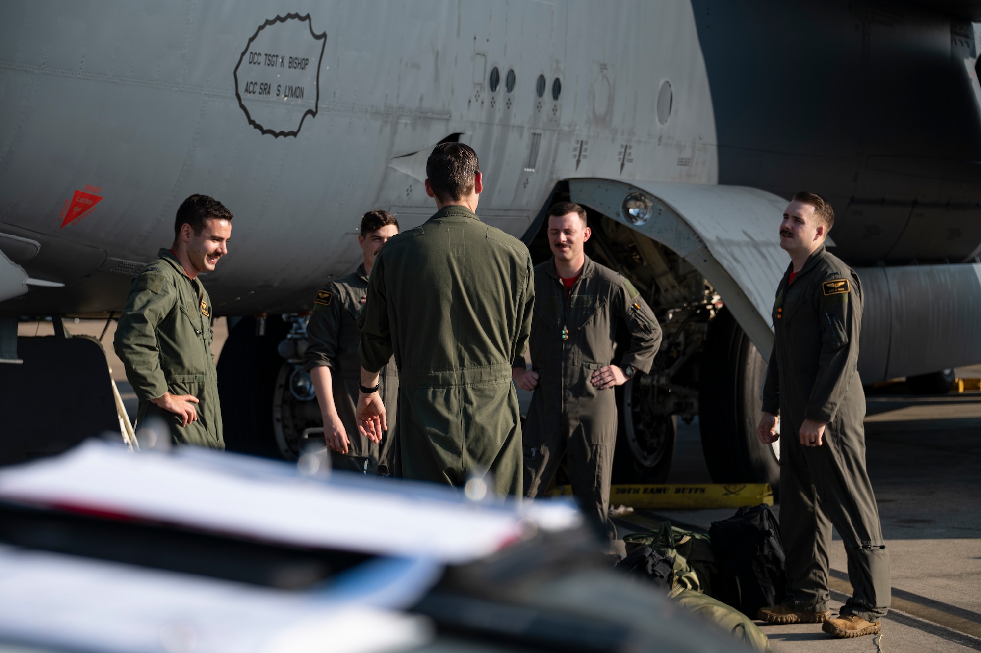Five men stand in a circle near an airplane.