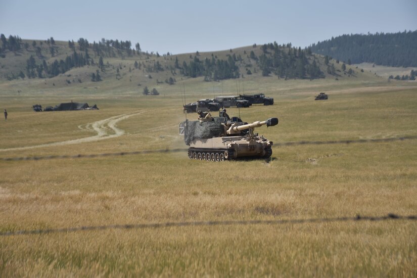 A military tank travels through a grassy area.