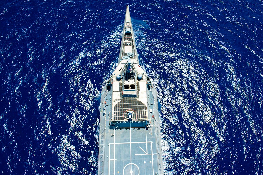 An aerial view of part of a military ship in deep blue water.