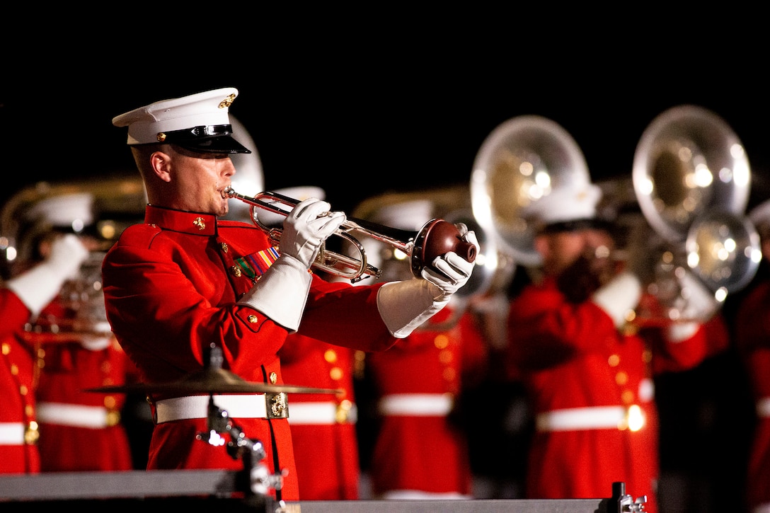 A Marine bugler performs with fellow musicians standing in the background.