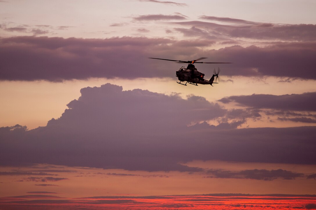 A helicopter flies against a colorful sky.