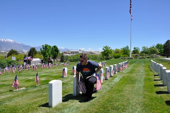 Sgt. Maj. Keith Moon places flags along headstone markers in the Veteran Memorial Cemetery at Camp Williams, Utah, May 31, 2021.