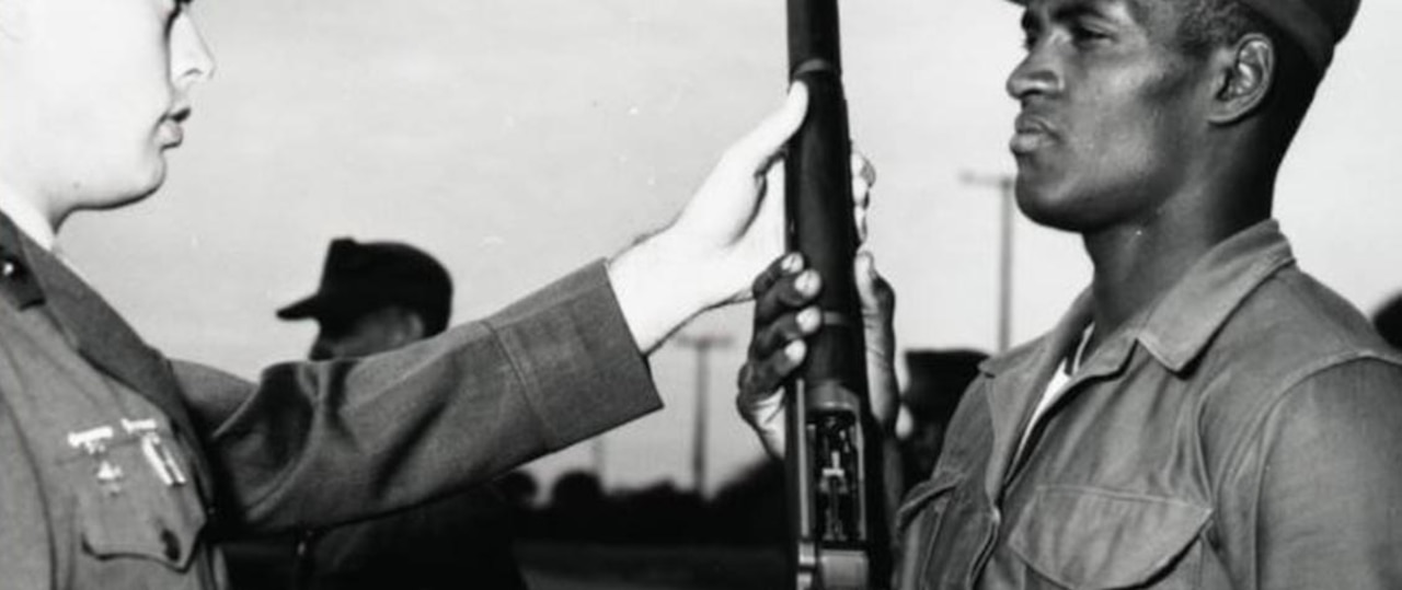 Two Marines stand facing each other, one holds a rifle while the other inspects it.