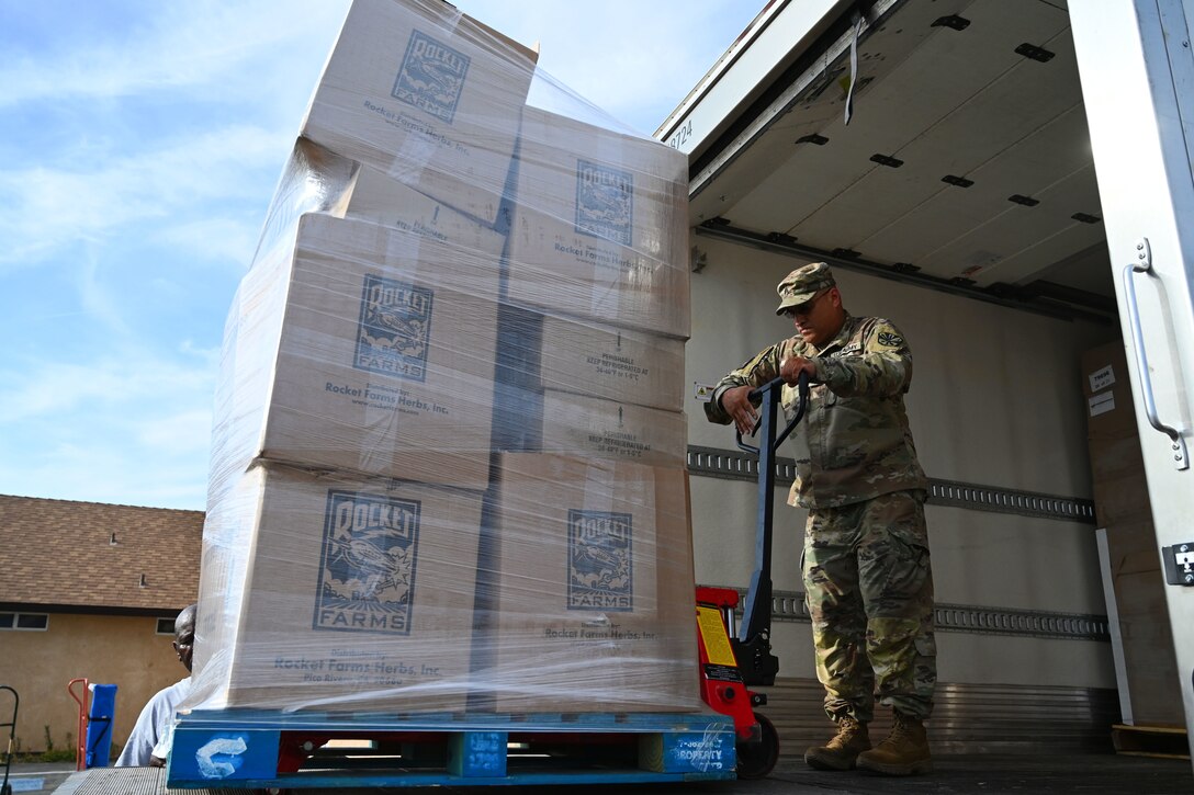 A soldier uses a forklift to unload pallets of grocery donations from a truck.