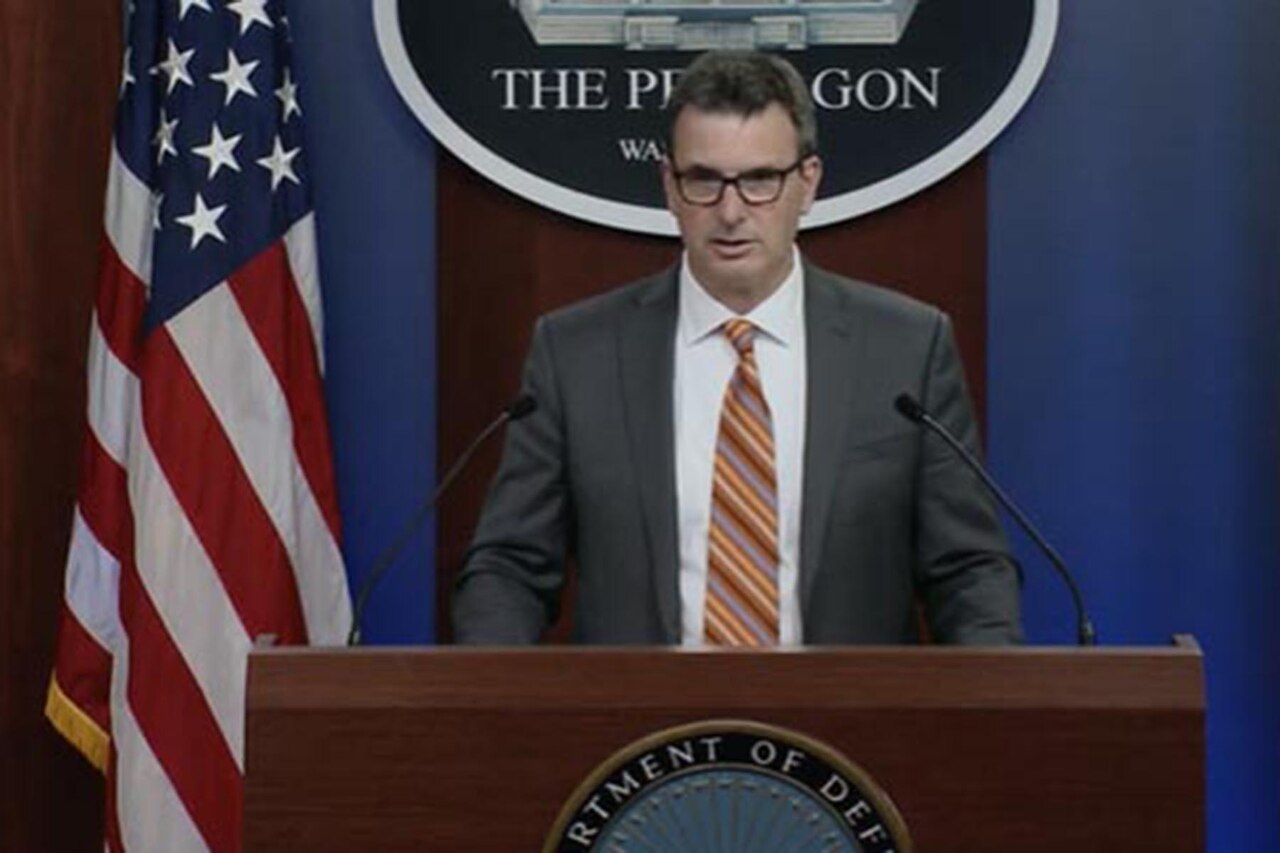 A man stands at a podium with a U.S. flag in the background.