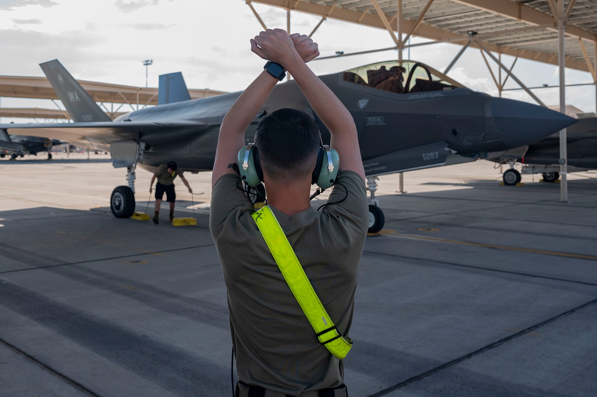 crew chief with hands in air with wrists crossed to the side of an F-35 on the flight line